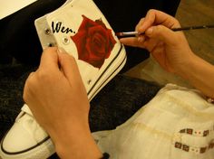 a woman is painting a rose on her white purse with black writing and holding a brush