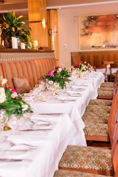 a long table with white linens and flowers on it in a fancy restaurant setting