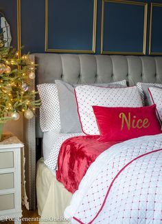 a bed with red and white pillows next to a small christmas tree in a room