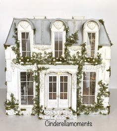 a white doll house with ivy growing on the front and side doors, windows, and shutters