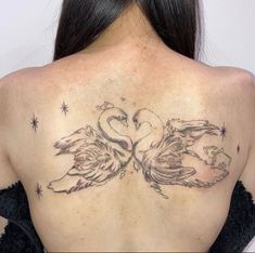 the back of a woman's shoulder with two swans on it and stars in the background