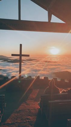 people sitting on benches looking out over the clouds at sunset with a crucifix in the foreground