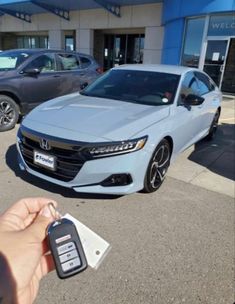 a person holding a car key in front of a honda dealership with other cars