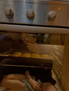 a woman taking a photo of some cupcakes in the oven with her cell phone