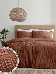 a bed with a brown comforter next to a potted plant and hanging wicker lamp