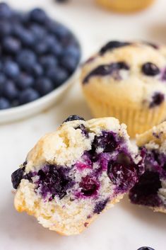 blueberry muffins cut in half on a white surface with bowl of blueberries