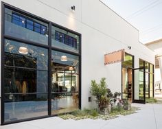 the front entrance of a building with large windows and plants in pots on the sidewalk