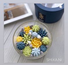 a bowl filled with lots of different colored flowers on top of a table next to a blue box