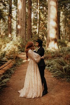 a bride and groom standing in the middle of a forest holding each other's arms