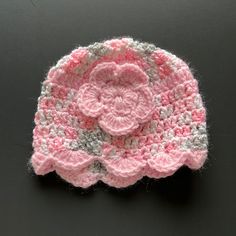 a crocheted pink and white hat on a black surface with a flower in the center