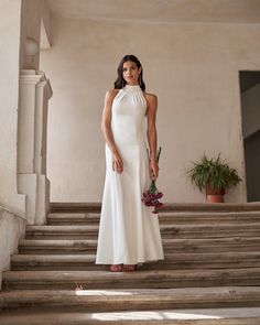 a woman in a white dress standing on some steps holding a flower bouquet and looking at the camera