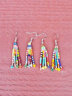 three pairs of multicolored beaded tassel earrings on a pink background,