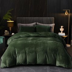 a bed with green comforter and pillows in a dark room next to a lamp