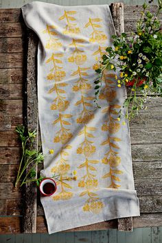 a tea towel with yellow leaves on it next to some flowers and a cup of coffee