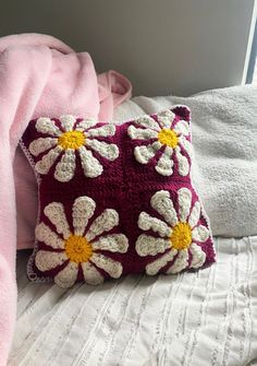 a crocheted pillow sitting on top of a bed next to a pink blanket