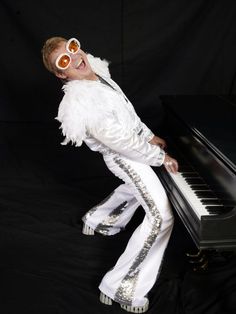 a young boy dressed in elvis clothing and sunglasses, standing next to a black piano