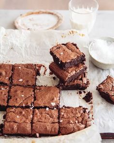 chocolate brownies cut into squares on top of parchment paper next to milk and spoons