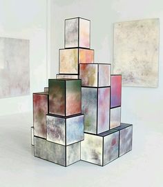 an abstract sculpture made out of squares in a room with two paintings on the wall