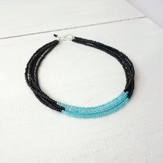 Multi strand seed bead choker necklace black aqua blue. Beaded layered necklace where five strands of seed beads are made in two colors - black and aqua blue or light turquoise. All strands have black seed beads on the sides towards the neck and the blue beads in the middle in front. The blue seed beads have a transparent top and a colored interior which makes them have an extra sparkly effect. The five strands are of a slightly different length so that the layers don't fall exactly on top of ea Layered Beaded Necklace, Choker Necklace Black, Layered Beaded Necklaces, Transparent Top, Beads Choker, Layered Choker Necklace, Black Choker Necklace, Bead Choker, Black Seed