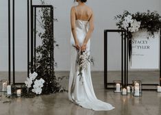 a woman in a wedding dress standing next to a floral arch with candles and flowers