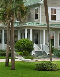 a hammock between two palm trees in front of a large house with porches