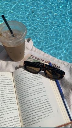 an open book, sunglasses and drink sitting on a towel next to a swimming pool