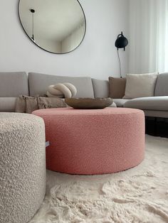 a living room with a couch, ottoman and round mirror on the wall above it