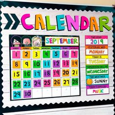 a colorful calendar is hanging on the wall in front of a bulletin board with writing and numbers