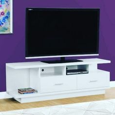 a flat screen tv sitting on top of a white entertainment center next to a purple wall