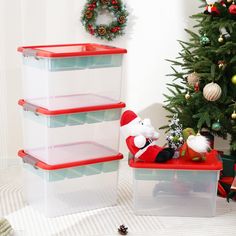 three plastic storage containers sitting next to a christmas tree