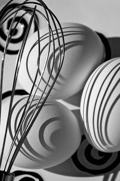 black and white photograph of balls in a vase with wire whisks on it