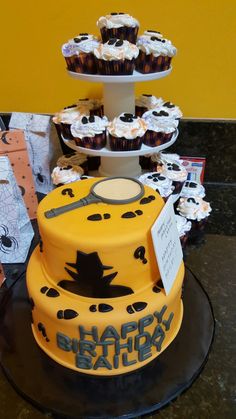 a yellow and black birthday cake with cupcakes on it