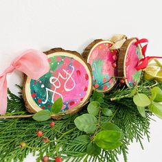 some ornaments are sitting on top of green branches and pine cones with pink bows around them