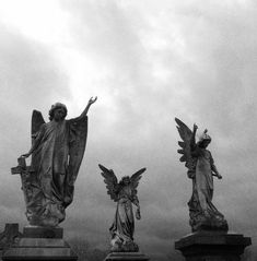 three statues with angel wings on top of each one in front of a cloudy sky