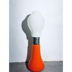 an orange and white lamp sitting on top of a cement floor next to a wall