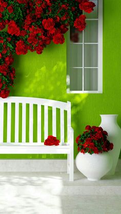 a white bench sitting in front of a green wall with red flowers growing on it