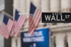 a wall street sign hanging from the side of a building with american flags in the background