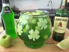 a glass filled with green liquid next to two bottles and an apple on a counter