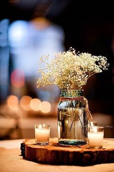 a vase filled with white flowers sitting on top of a wooden table next to candles