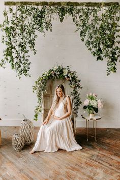 a woman sitting on a chair in front of a wall with greenery and flowers