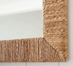 a close up of a mirror on a wall with wicker frame and white tiles