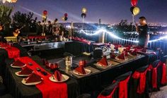 an outdoor dining area with red and black table cloths, candles and plates on the tables