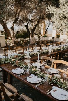 an outdoor table set up with place settings and greenery on the tables for dinner