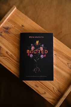 a book sitting on top of a wooden table next to a piece of wood with the word rooted written on it