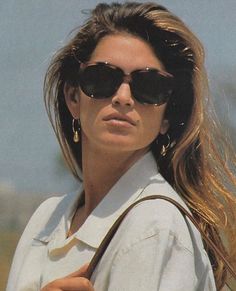 a woman wearing sunglasses and carrying a brown purse on her shoulder, looking off to the side