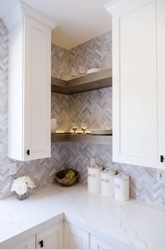 a kitchen with white cupboards and marble counter tops in front of a wallpapered herringbone backsplash