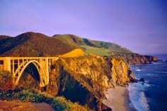 a bridge over the ocean on top of a cliff with mountains in the back ground