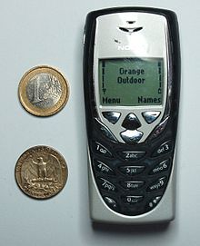 an old cell phone sitting next to two coins and a coin clipping on the wall