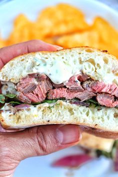 a hand holding a sandwich with meat, cheese and lettuce in front of some fries