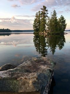 a large rock sitting on top of a lake next to a shore covered in trees